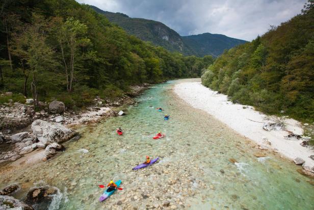 Mehrere Kajakfahrer paddeln auf einem klaren Fluss durch eine bewaldete Landschaft.