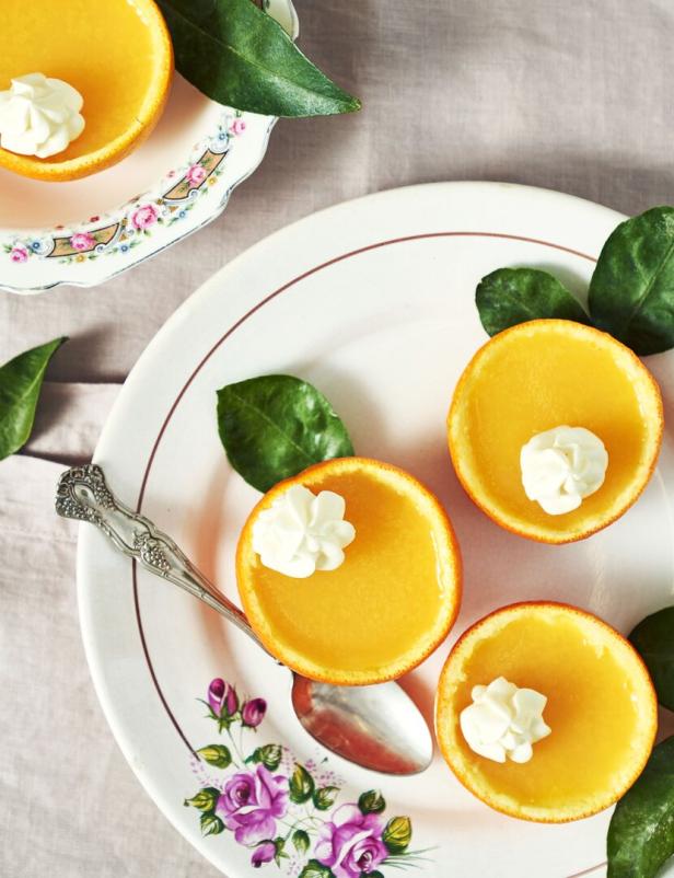 Orangenhälften, gefüllt mit Pudding und einem Klecks Sahne, auf einem Teller mit floralem Muster.