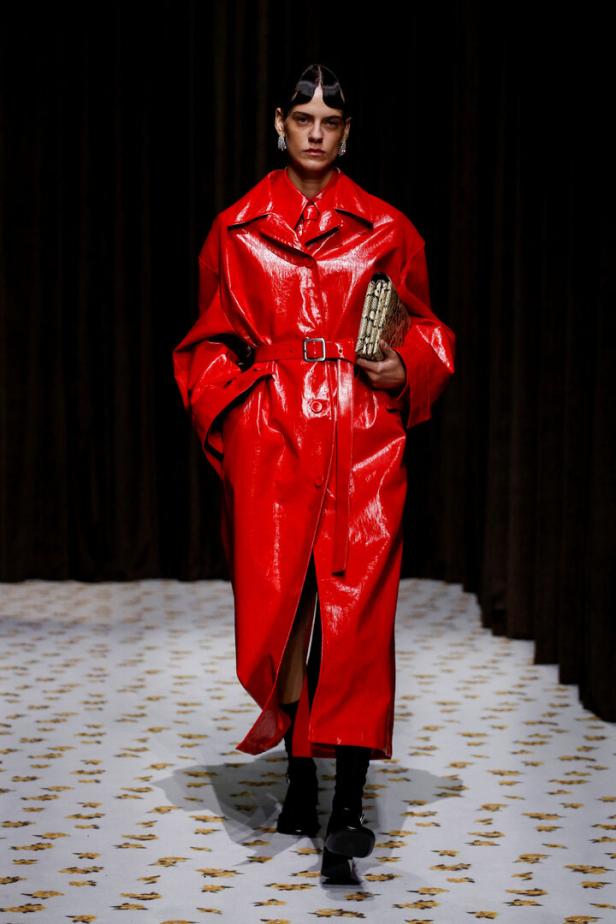 Ein Model in einem glänzenden roten Trenchcoat auf einem Laufsteg.