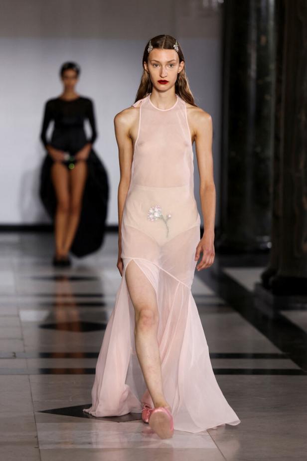 Eine Frau in einem transparenten, rosa Kleid mit Blumenapplikation auf einem Laufsteg.
