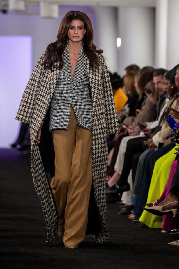 Eine Frau auf dem Laufsteg trägt einen Hahnentrittmantel über einem Blazer und einer Hose.