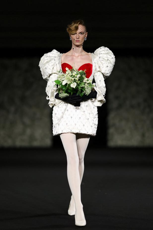 Ein Model mit Schleier und weißem Kleid mit Puffärmeln hält einen Blumenstrauß.
