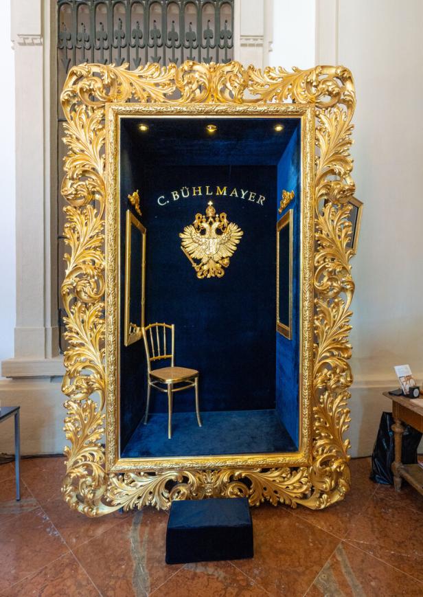 Ein goldener Stuhl in einer Nische mit blauem Samt, gerahmt von einem verzierten Goldrahmen von C. Bühlmayer.