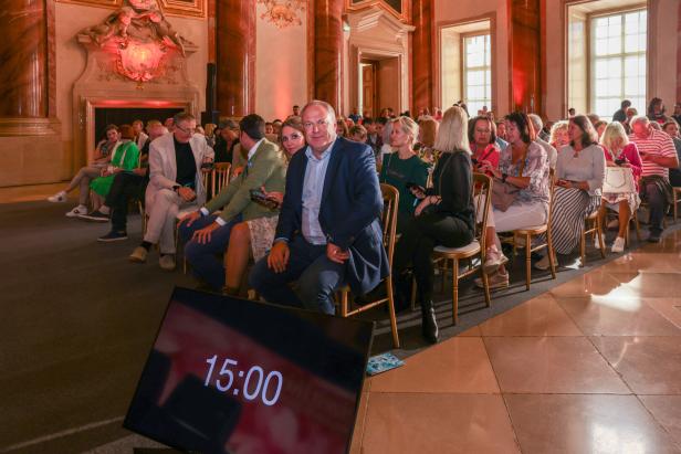 Zahlreiche Menschen sitzen in einem Saal und warten auf den Beginn einer Veranstaltung.