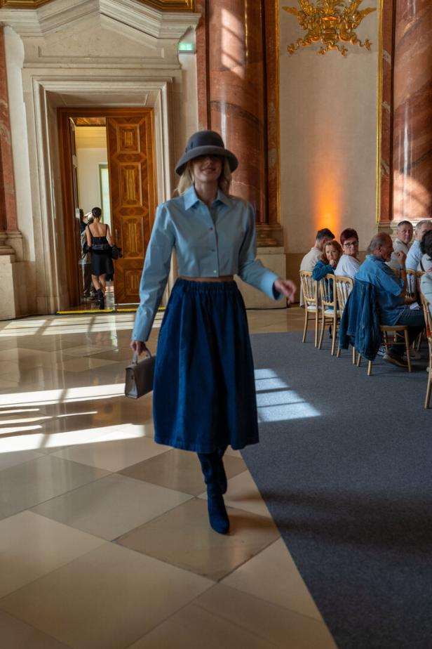 Eine Frau mit Hut, blauem Hemd und Rock geht in einem eleganten Raum.