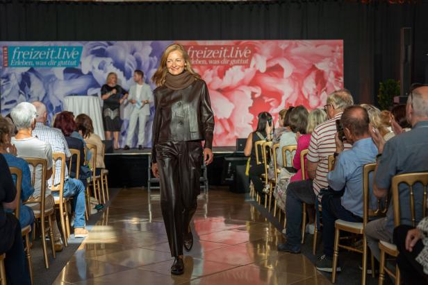 Eine Frau in brauner Lederkleidung läuft auf einem Laufsteg vor Publikum.