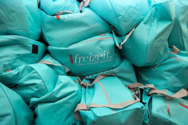 Ein Stapel türkisfarbener Taschen mit dem Aufdruck „freizeit.at“.