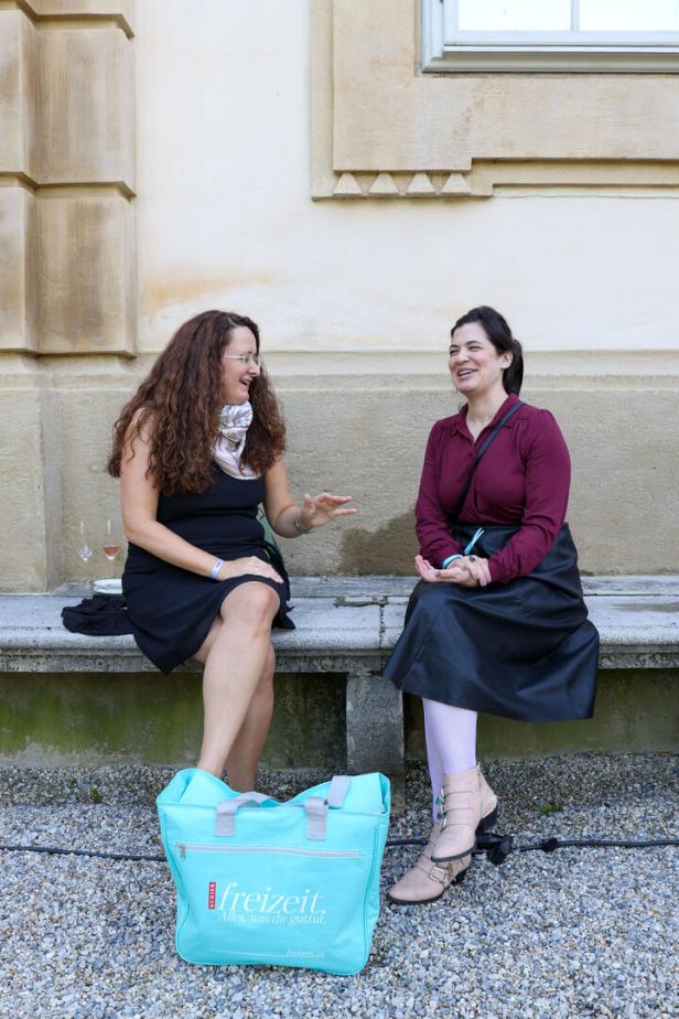 Zwei Frauen sitzen auf einer Bank und unterhalten sich.