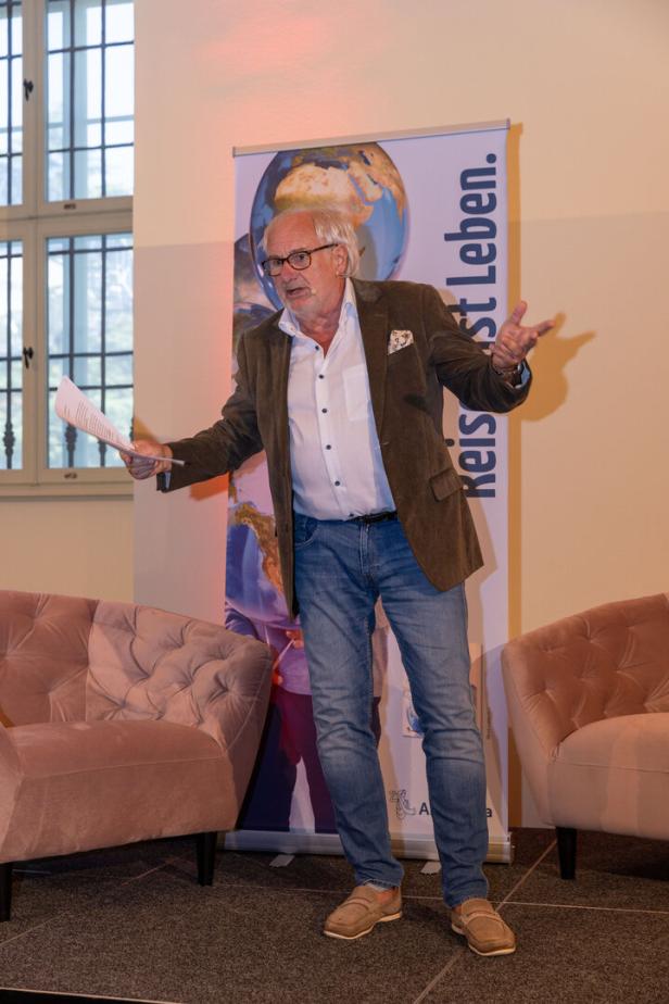 Ein Mann mit Brille gestikuliert auf einer Bühne mit einem Dokument in der Hand.