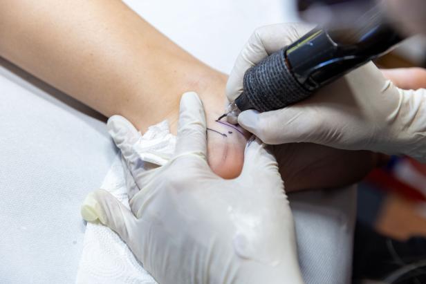 Eine Person bekommt ein Tattoo auf den Fußrücken gestochen.