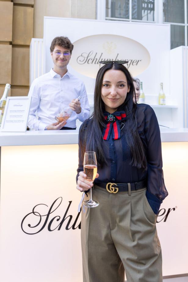 Eine Frau hält ein Glas Sekt vor einem Schlumberger-Stand.