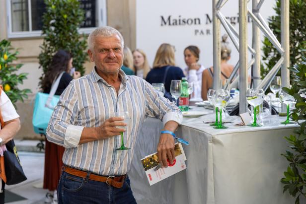 Ein Mann mit Drink steht an einem Tisch bei einer Veranstaltung von Maison Margiela.