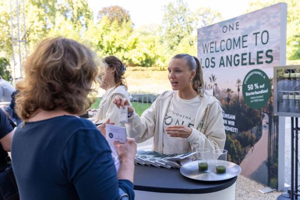 Eine junge Frau präsentiert ein Produkt von Biogena ONE auf einem Stand mit dem Slogan „Welcome to Los Angeles“.