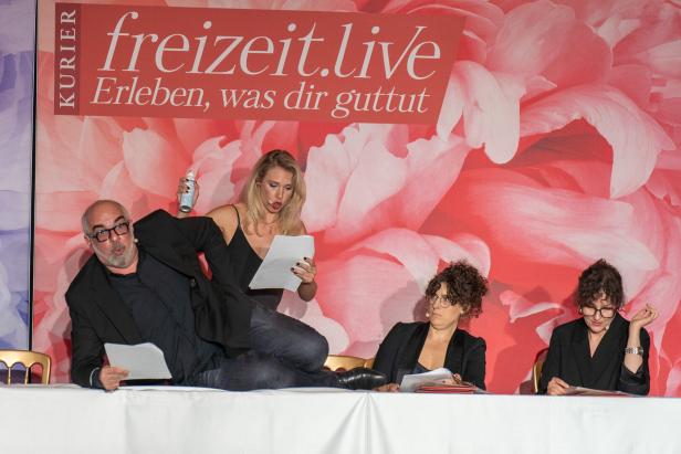Michael Niavarani liegt am Tisch, Jenny Frankl steht empört hinter ihm.