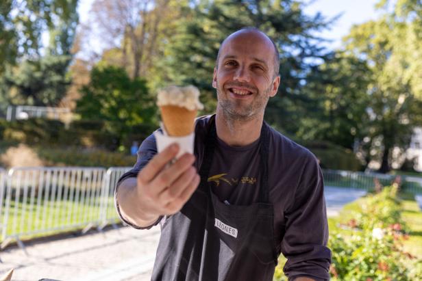 Ein lächelnder Mann im Park präsentiert ein Eis in der Waffel.