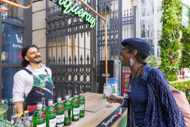 Eine Frau hält ein Getränk an einer Tanqueray-Bar und lacht mit einem Barkeeper.