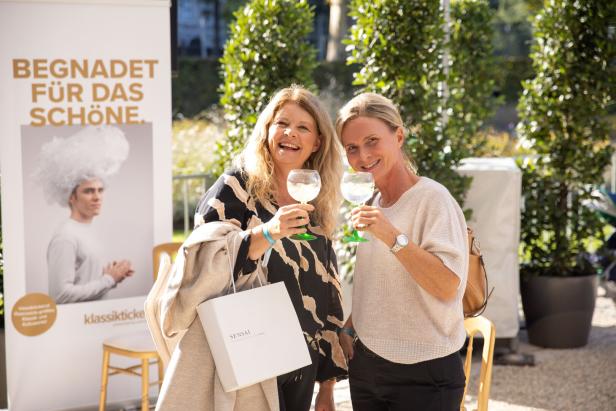 Zwei Frauen stoßen im Freien mit Gin Tonic an.