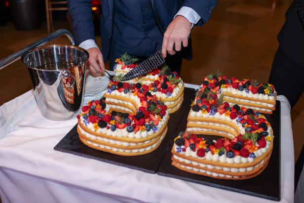 Ein Mann schneidet eine Torte in Form der Zahl 5, dekoriert mit Beeren und Blüten.