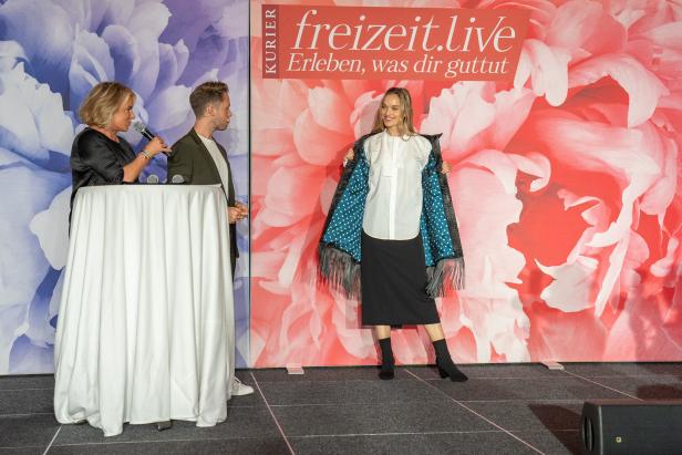 Eine Frau präsentiert eine Jacke mit blauem Innenfutter und weißen Punkten auf einer Bühne.