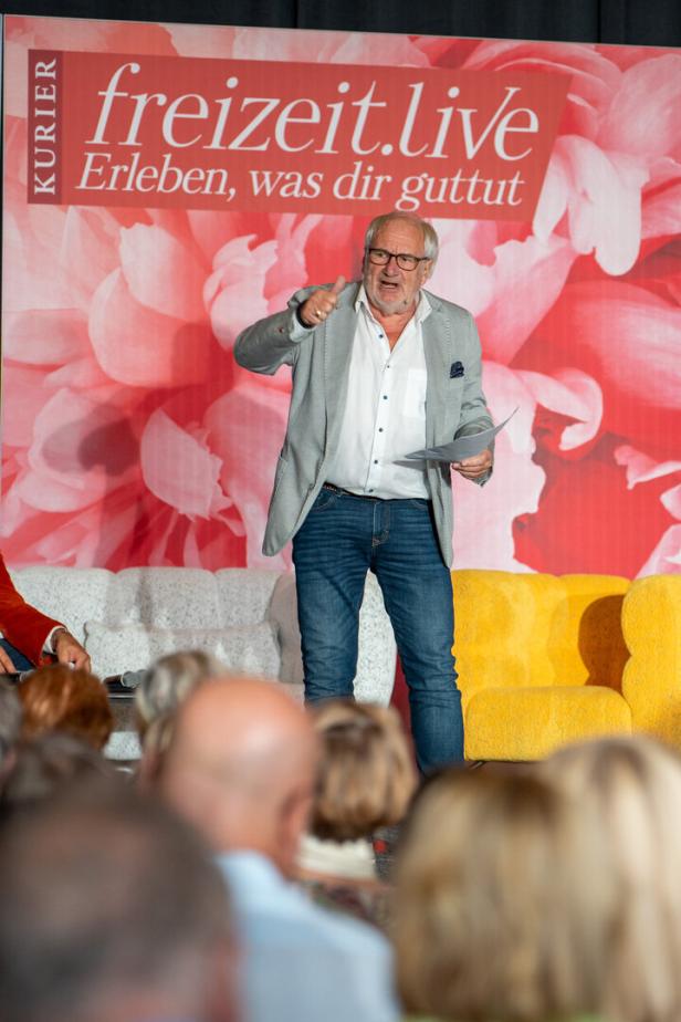 Ein Mann steht auf einer Bühne vor einem Publikum und gestikuliert.
