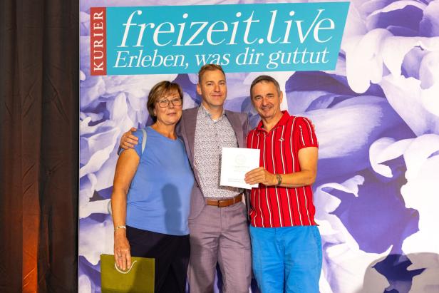 Drei Personen posieren vor einem „freizeit.live“-Banner mit Blumenmuster.