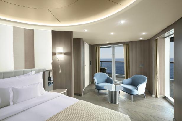 Ein helles, modernes Hotelzimmer mit Meerblick und blauen Sesseln.