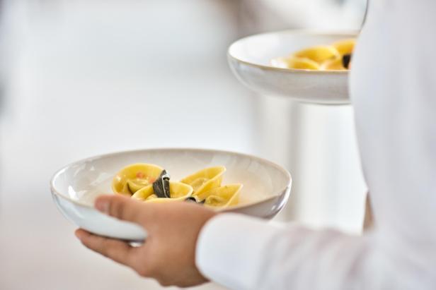 Ein Kellner serviert zwei Teller gefüllte Pasta mit Salbei.