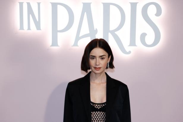 Lily Collins vor einer Wand mit der Aufschrift „In Paris“.