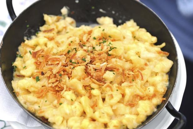 Käsespätzle mit Röstzwiebeln und Schnittlauch in einer schwarzen Pfanne serviert.