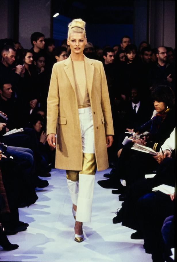 Linda Evangelista läuft auf dem Laufsteg in einem beigen Mantel und weißen Hosen.
