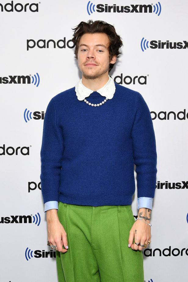 Harry Styles trägt einen blauen Pullover mit grünem Hose vor einem SiriusXM- und Pandora-Hintergrund.