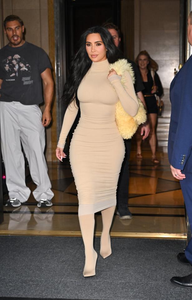 Kim Kardashian verlässt ein Gebäude in einem beigen Kleid und passenden Strumpfhosen.