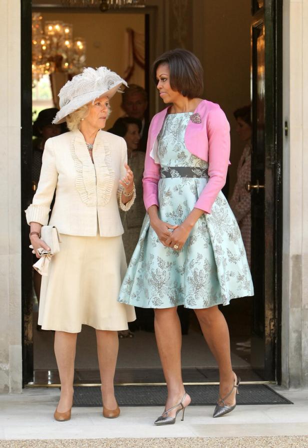 Camilla, Königin Gemahlin, und Michelle Obama stehen zusammen vor einer Tür.