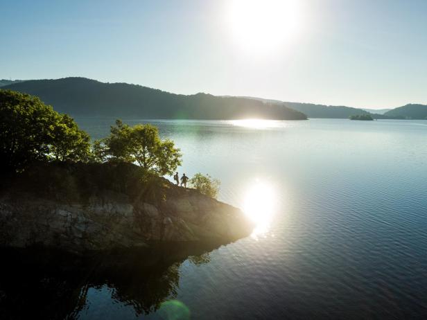 Zwei Personen stehen auf einem Felsen am Ufer eines Sees im Morgenlicht.