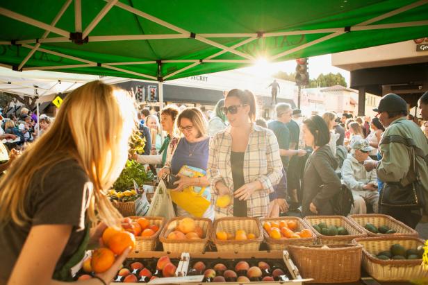 Auf einem Markt kaufen Menschen Obst und Gemüse an einem sonnigen Tag.