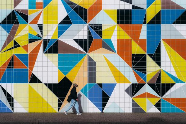 Eine Person geht vor einer Wand mit einem bunten, geometrischen Muster entlang.