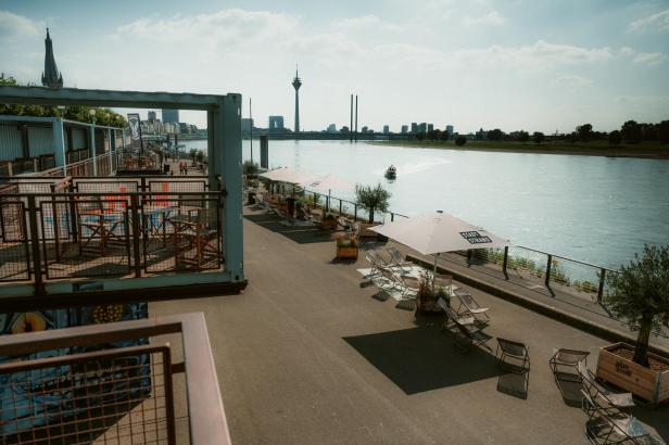 Ein Blick auf den Düsseldorfer Medienhafen mit dem Rheinturm und einem „Stadtstrand“ im Vordergrund.