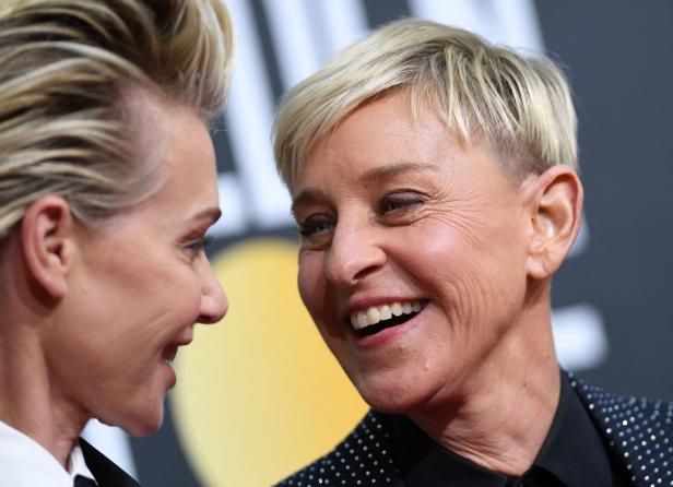 Ellen DeGeneres lächelt Portia de Rossi an, während beide vor einem dunklen Hintergrund stehen.