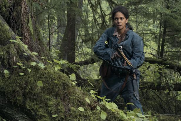 Eine Frau mit einer Armbrust steht in einem dichten Wald.