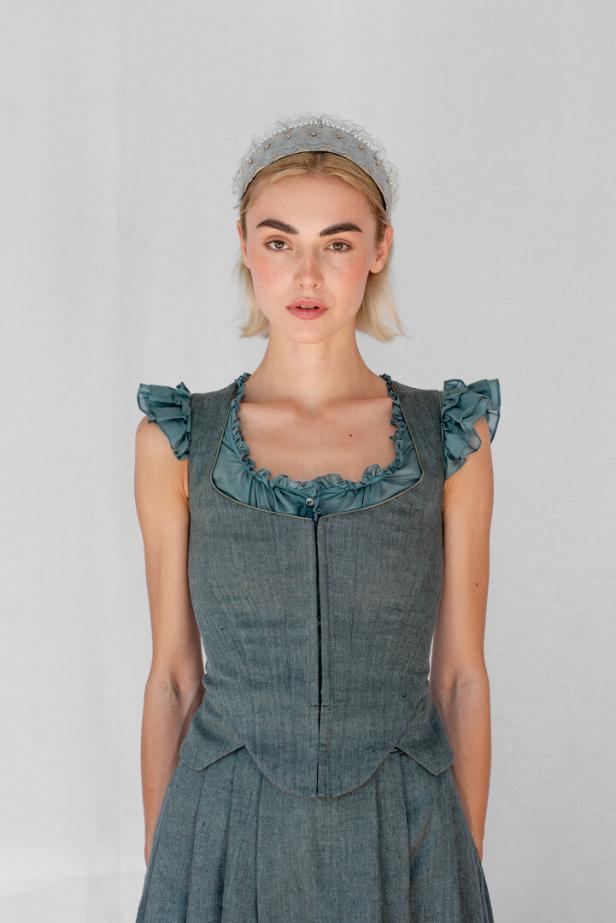Eine Frau mit blonden Haaren trägt ein blau-graues Kleid und ein verziertes Haarband.