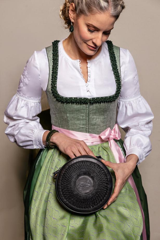Eine Frau im Dirndl hält eine runde, schwarze Handtasche.