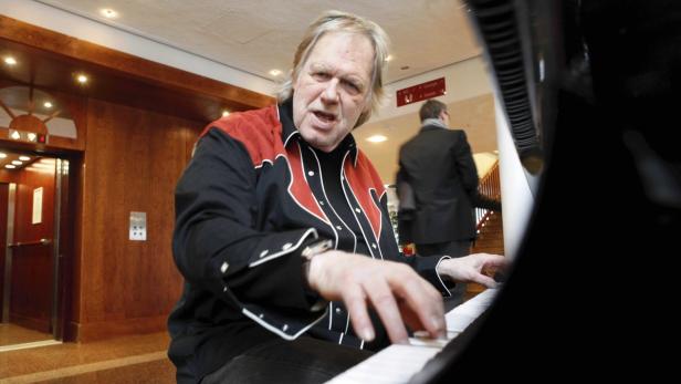 Ein Mann mit einem Cowboyhemd spielt Klavier in einem Gebäude.