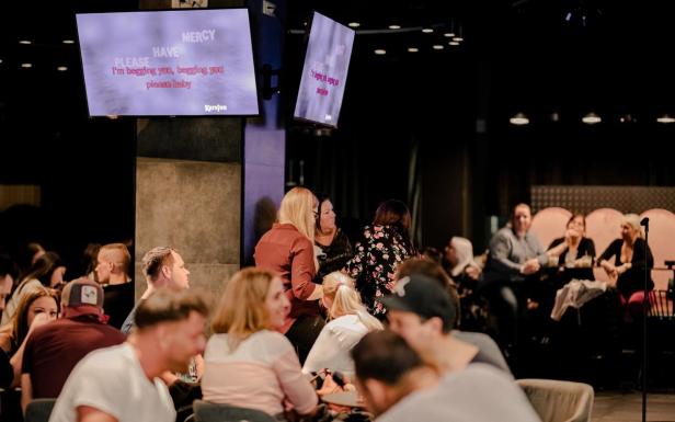 Menschen sitzen in einer Bar und singen Karaoke.