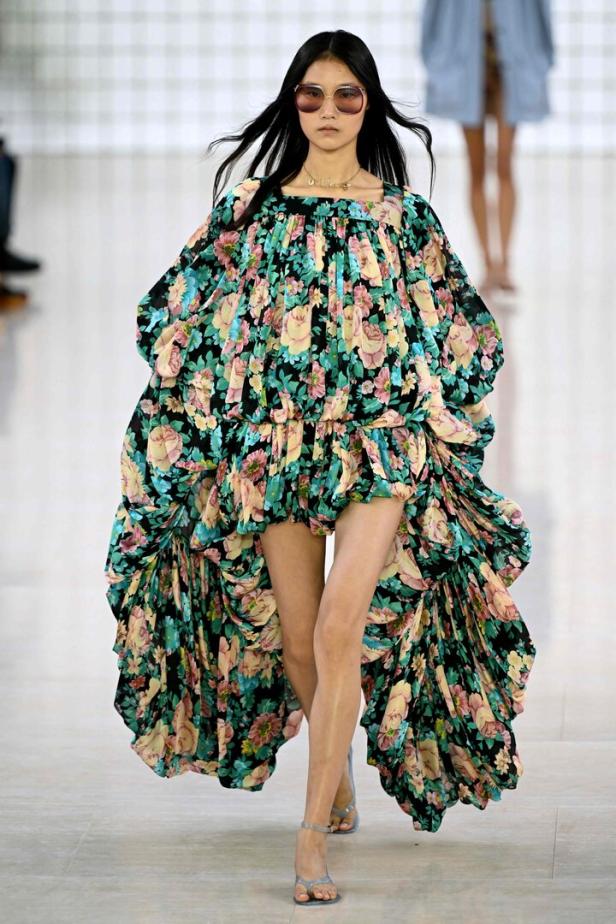 Eine Frau mit Sonnenbrille präsentiert ein blumengemustertes Kleid auf dem Laufsteg.