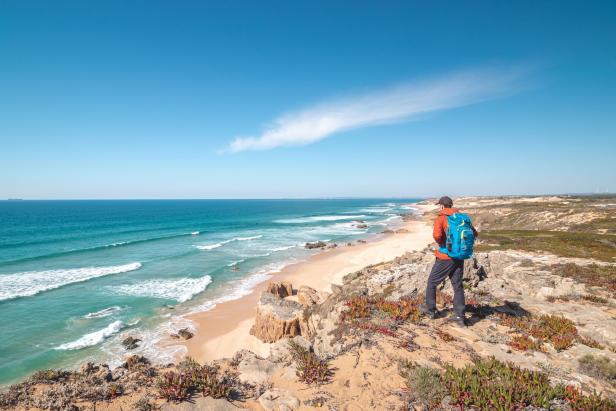 Ein Wanderer mit Rucksack blickt auf einen Strand und das Meer.