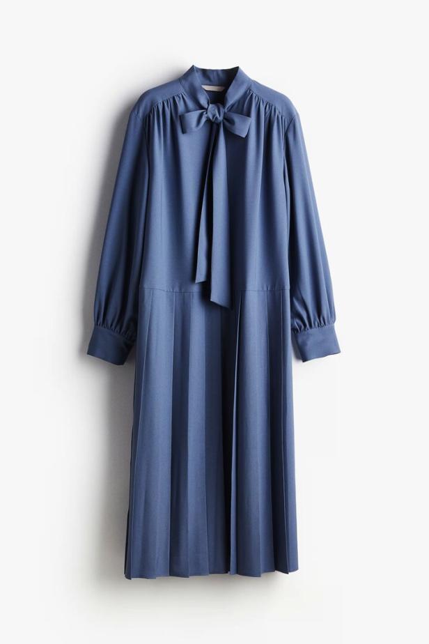 Ein blaues, plissiertes Kleid mit langen Ärmeln und einer Schleife am Kragen.