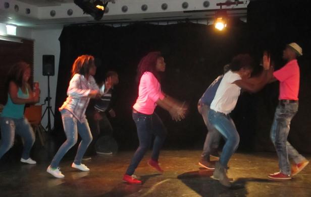 Eine Gruppe junger Leute tanzt auf einer Bühne unter dem Scheinwerferlicht.