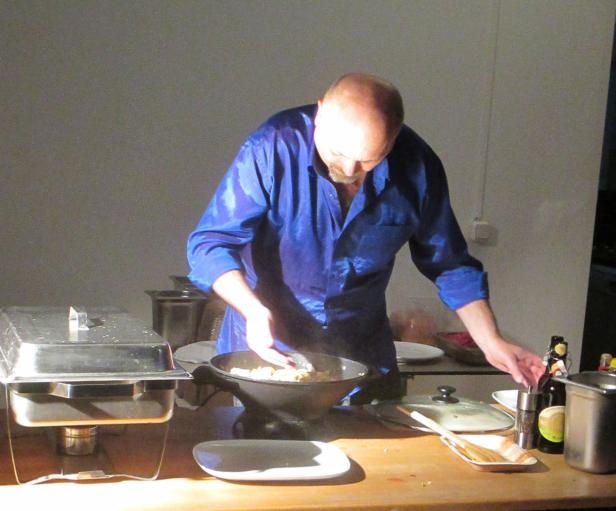 Ein Mann in einem blauen Hemd kocht in einer dunklen Küche.