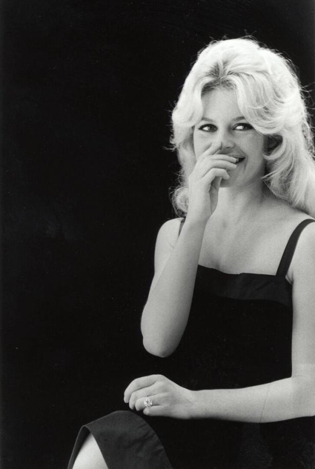 Brigitte Bardot lächelt und hält eine Hand vor den Mund.