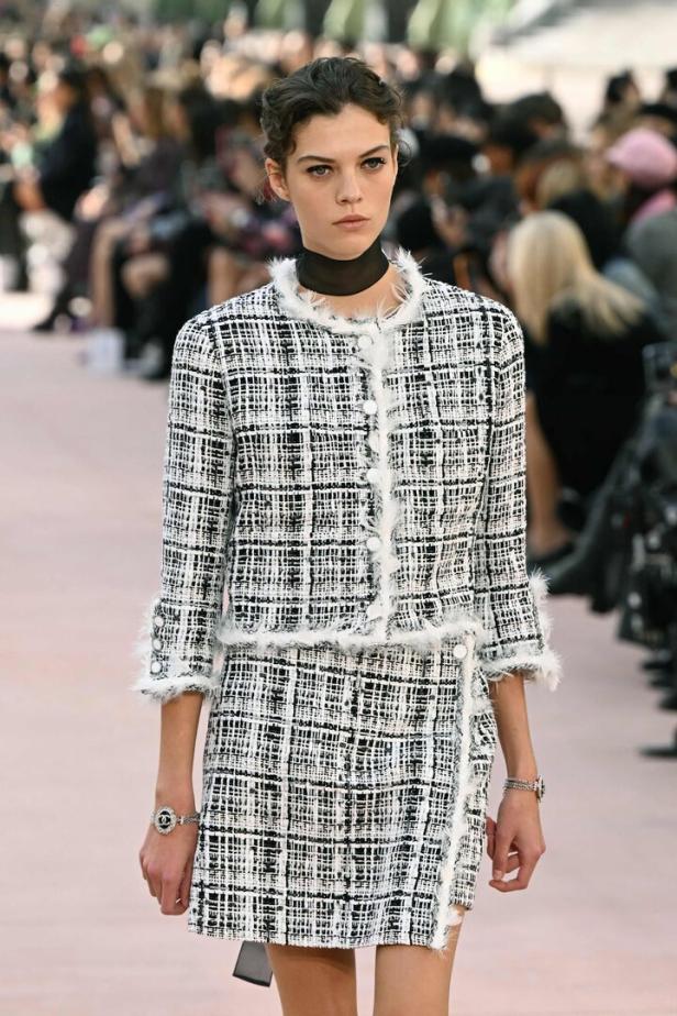 Ein Model präsentiert ein schwarz-weißes Tweed-Kostüm mit Fransen auf einem Laufsteg.